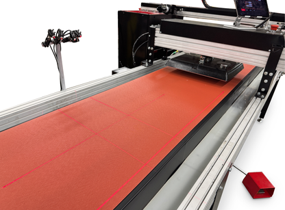 A large industrial laser cutter or engraving machine shown at an angle on a white background, with a red sheet of material on the bed and a small red handheld controller nearby.