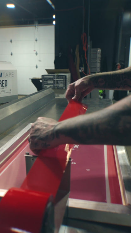 Video showing a person applying PMI Red Screen Printers Tape to the edges of a screen printing frame in a shop setting, demonstrating its easy application and secure seal.